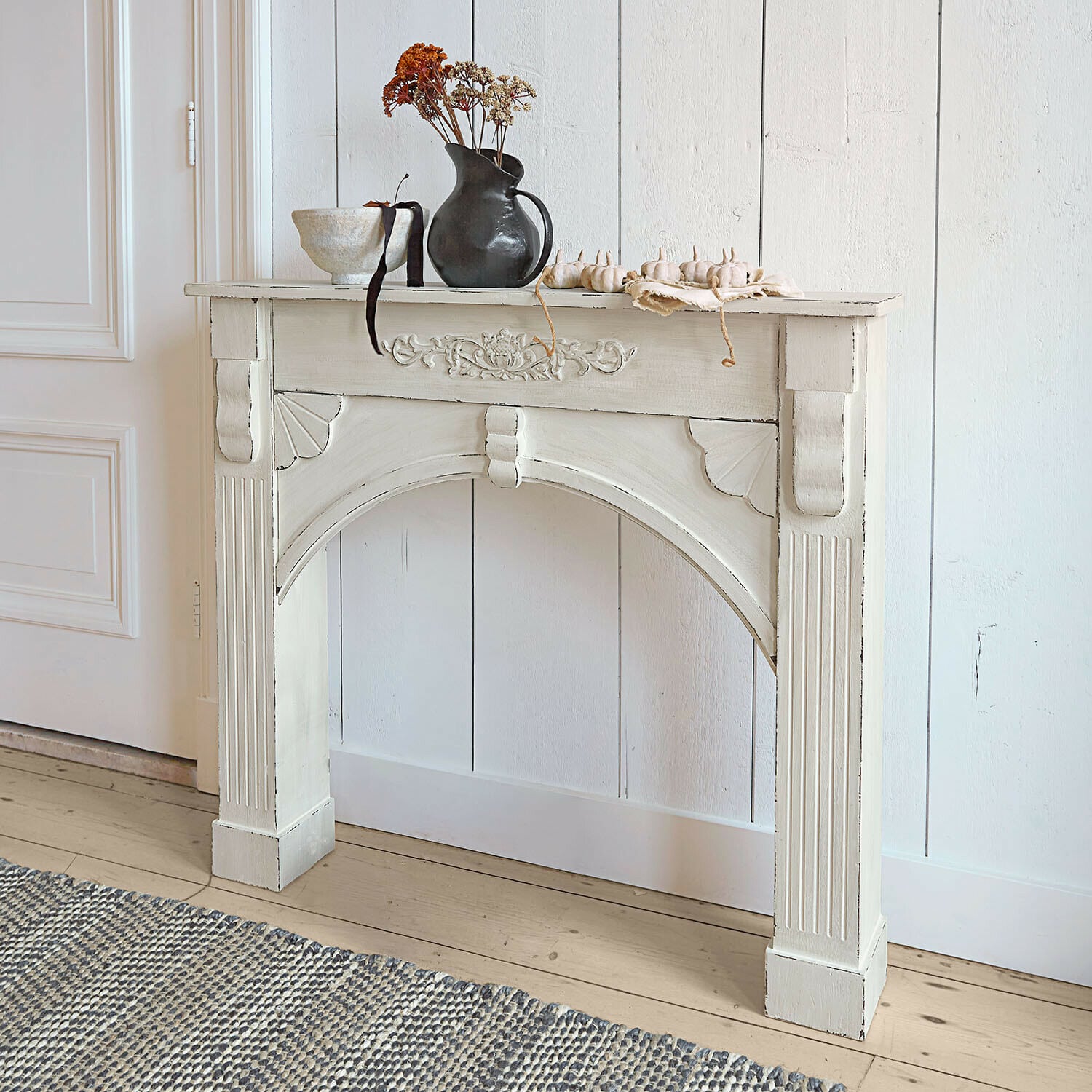 Consola de chimenea Maxwell Consola de madera blanca con tallados decorativos y jarrón negro con flores secas encima