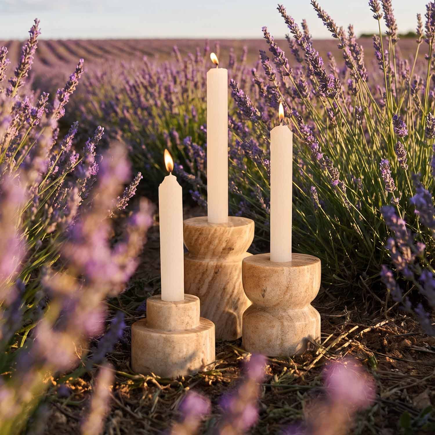 Tres velas crema en candelabros de madera natural en un campo de lavanda al atardecer