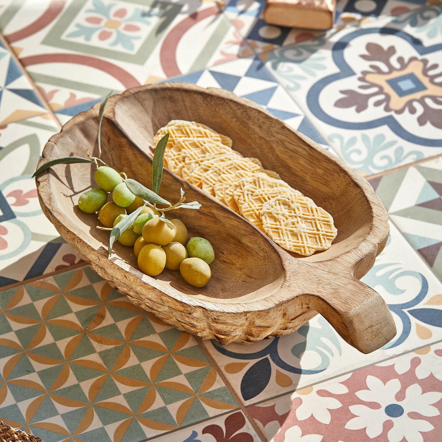 Cuenco Vinoros Cuenco de madera con asa con aceitunas verdes y galletas sobre azulejos coloridos