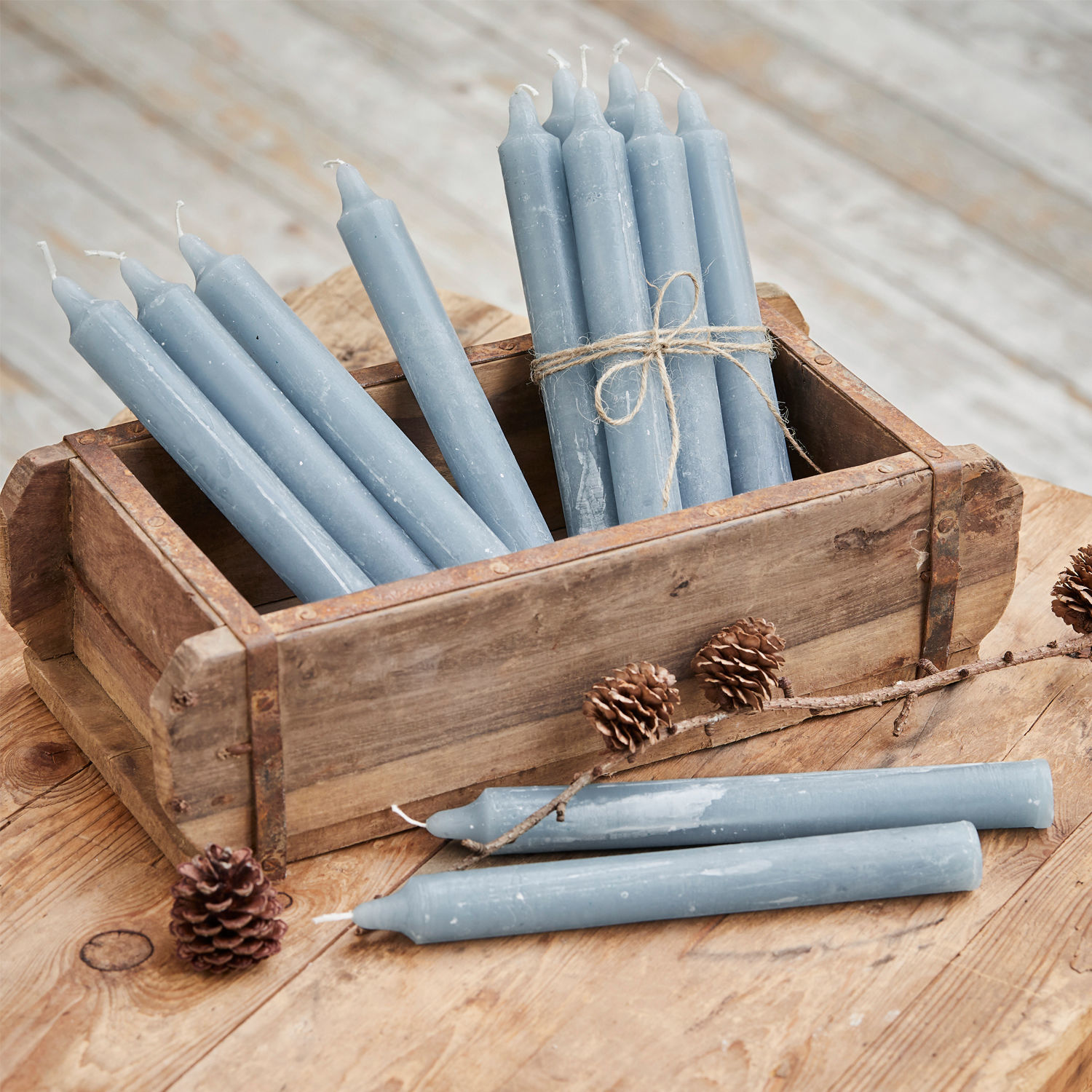 Set de 12 velas Bauceau Conjunto de velas azules de cera en caja de madera sobre mesa rústica con piñas