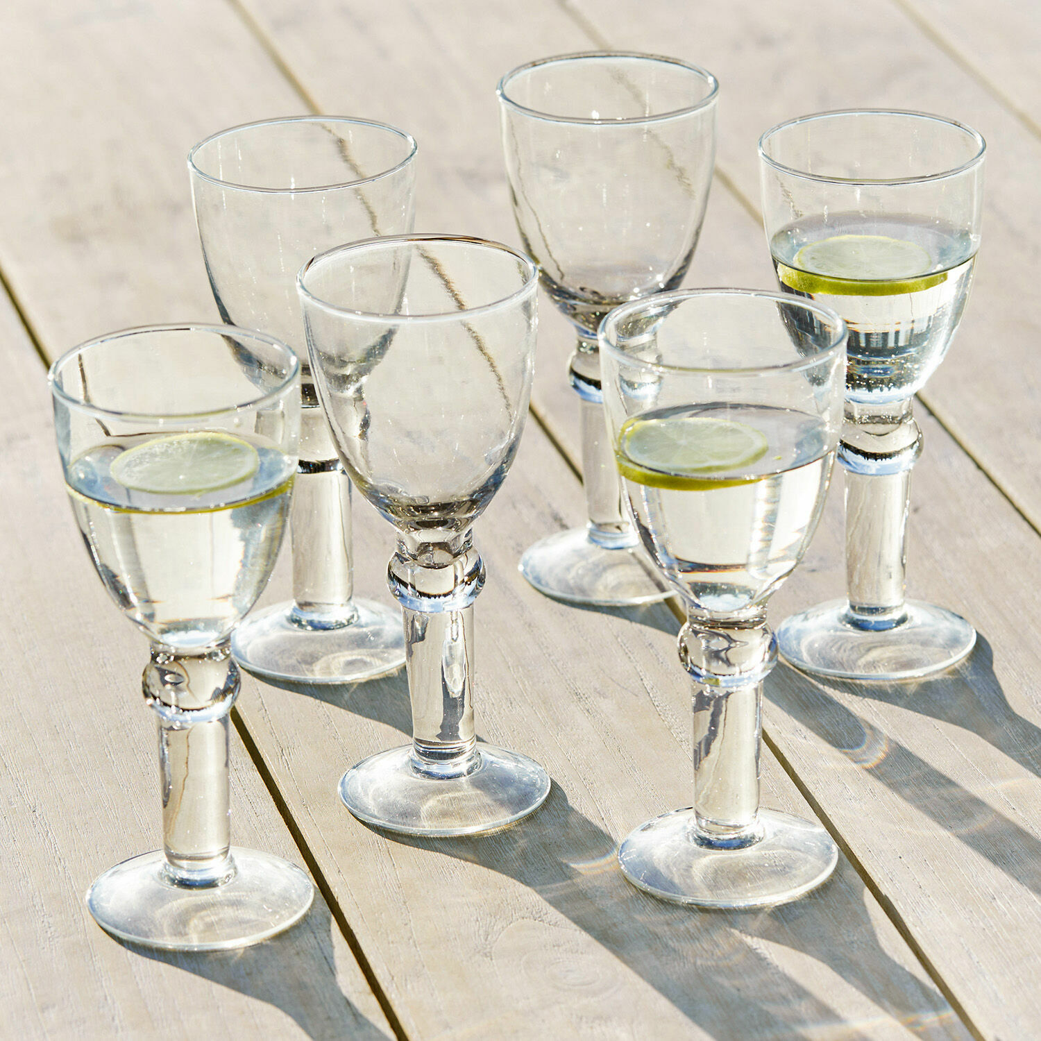 Set de 6 copas de vino Devon Conjunto de seis vasos transparentes con agua y rodajas de limón sobre mesa de madera clara