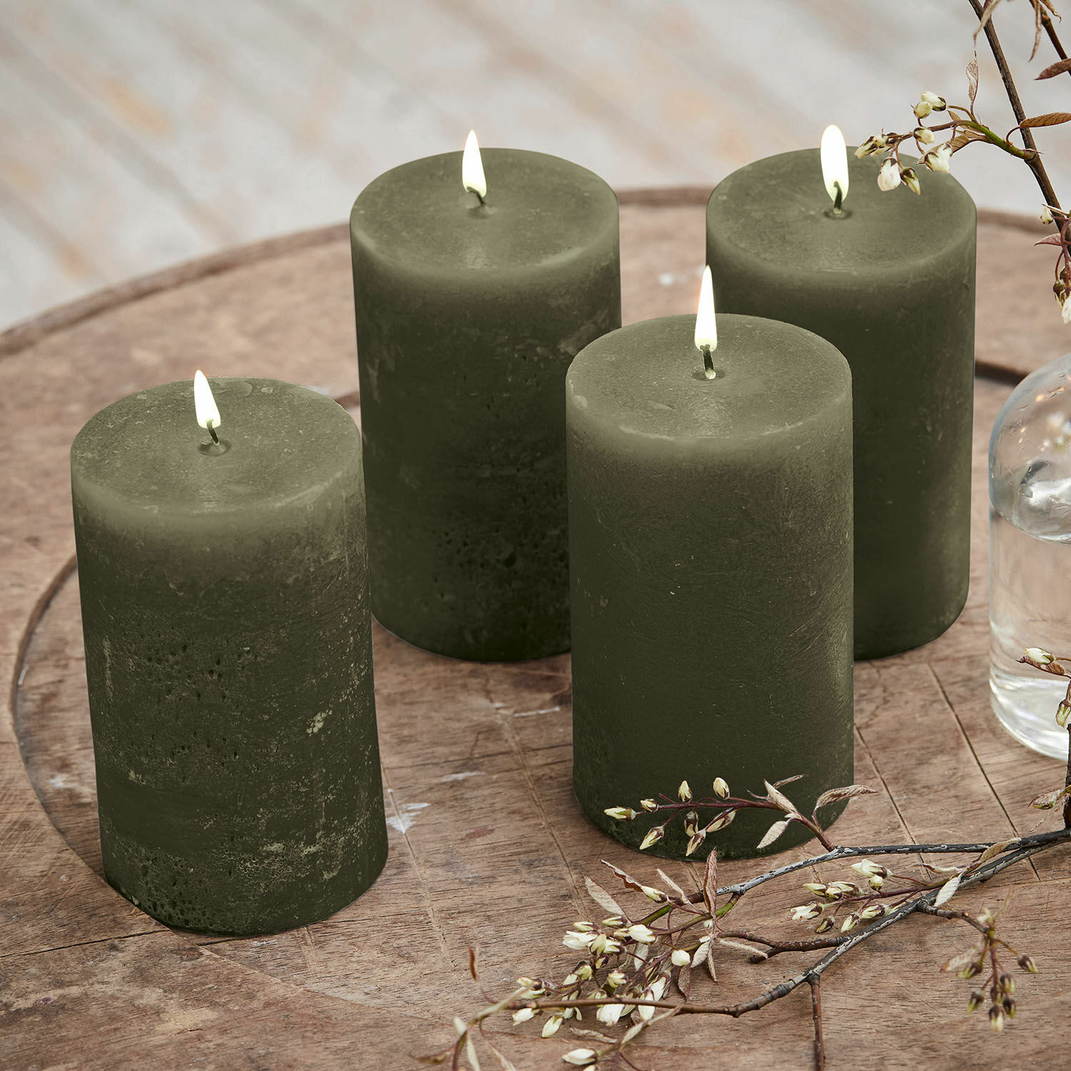 Set de 4 velas Braga Conjunto de cuatro velas verdes de cera sobre mesa de madera con decoración floral