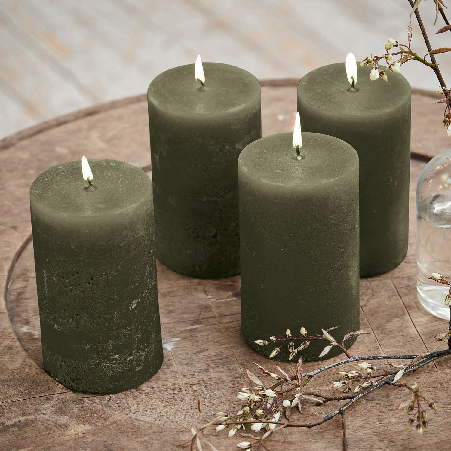 Set de 4 velas Braga Conjunto de cuatro velas verdes de cera sobre mesa de madera con decoración floral