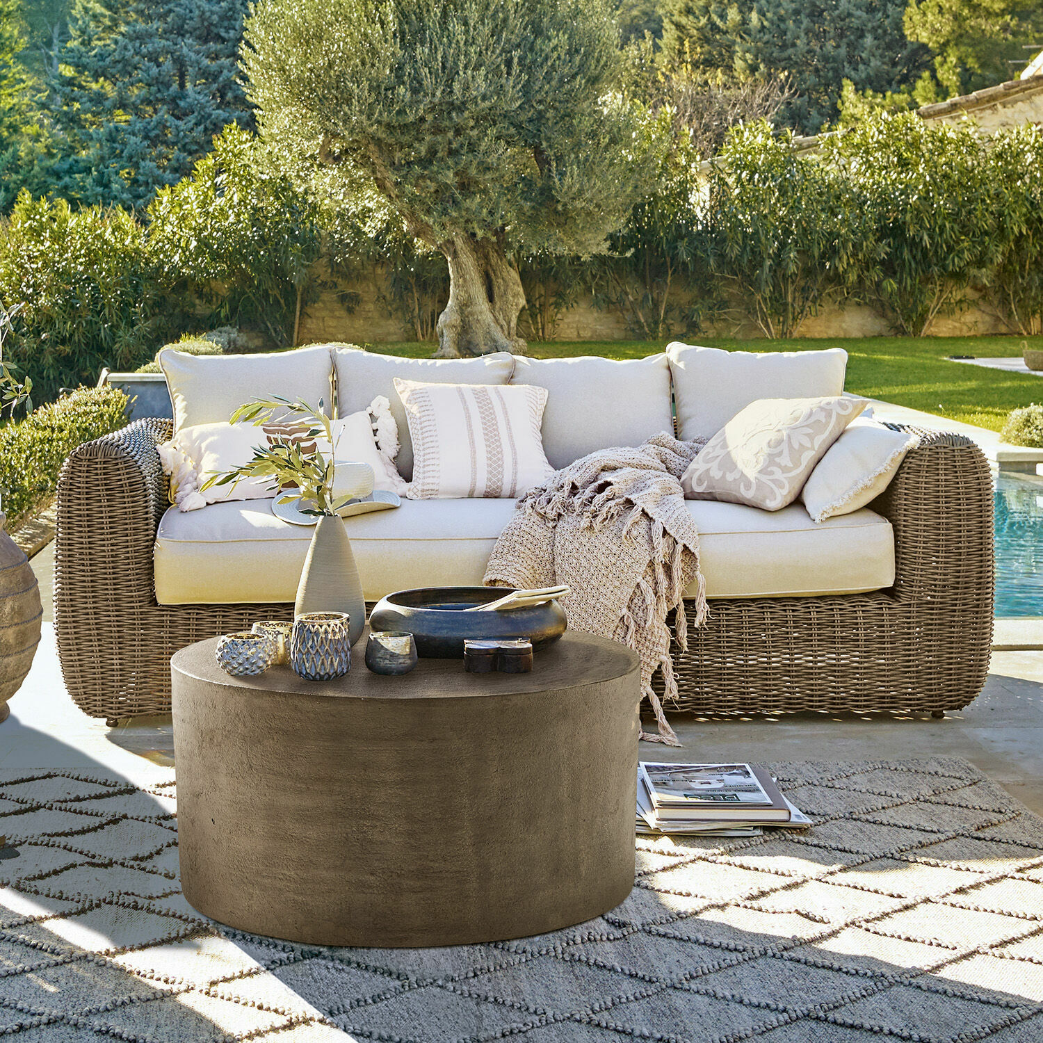 Sofá de jardín de ratán beige con cojines y mesa de centro redonda de hormigón en exterior