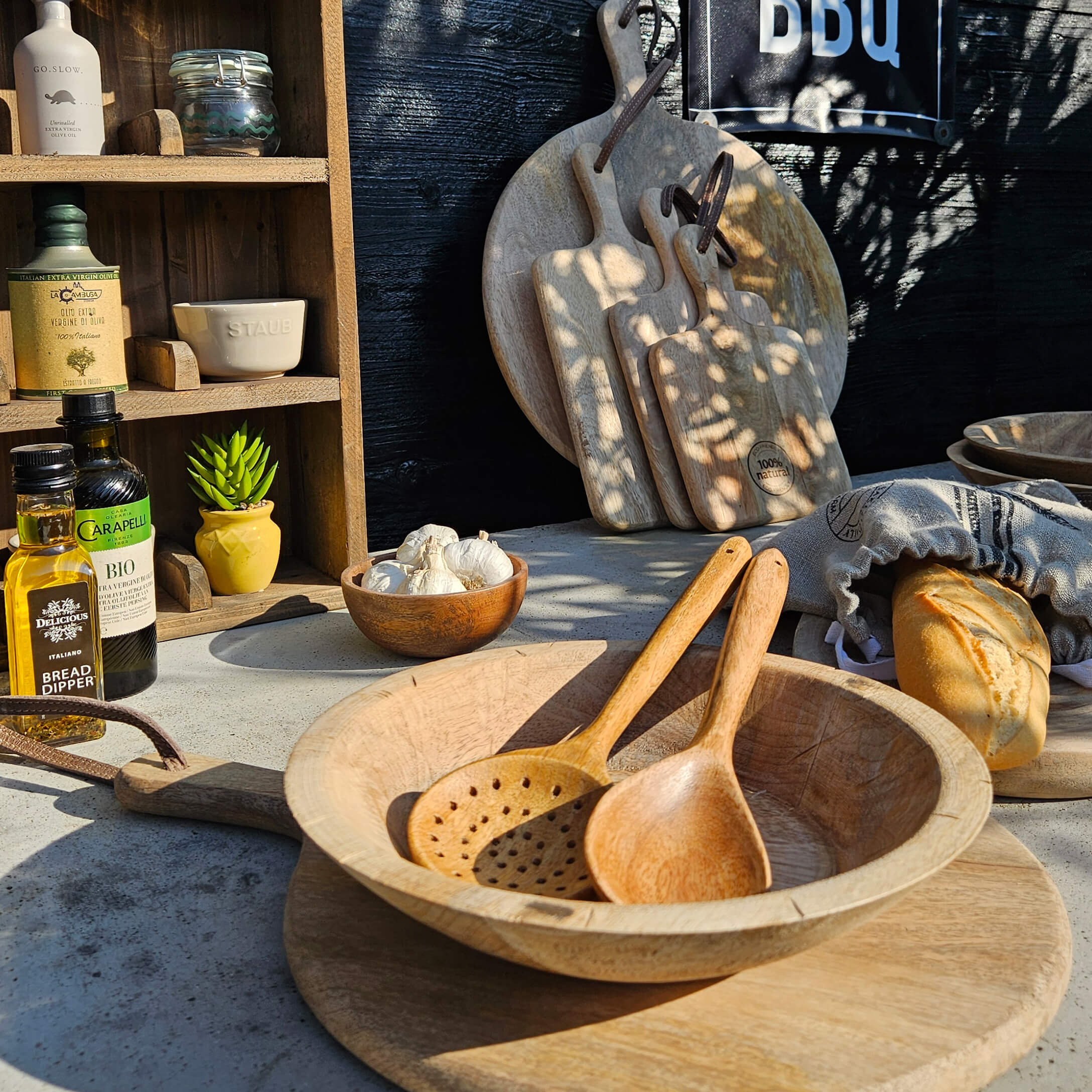Conjunto de tablas de cortar y cucharas de madera sobre mesa con pan y aceite de oliva