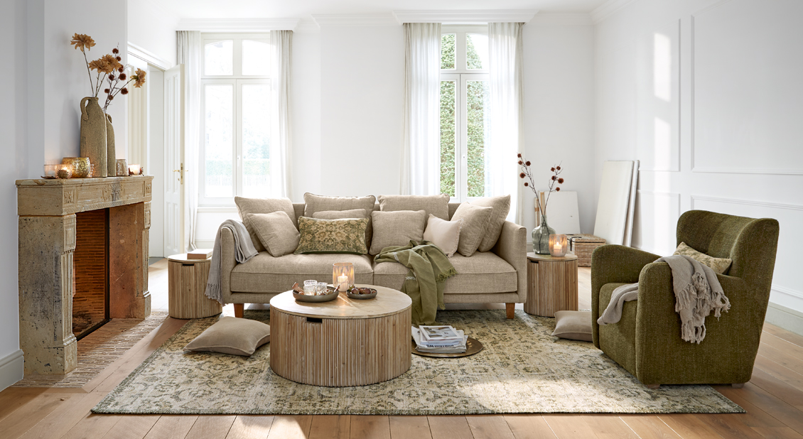Sala acogedora con sofá beige, sillón verde y mesas de madera sobre alfombra decorativa