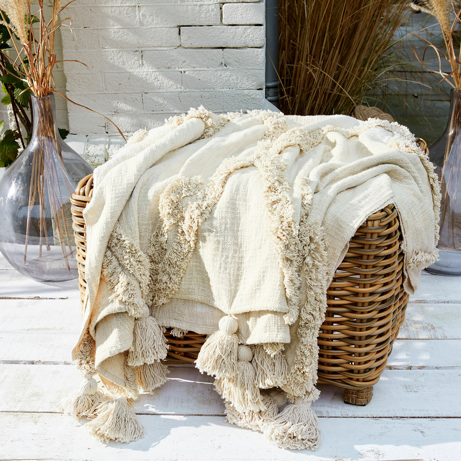 Plaid Linares Manta crema de algodón con borlas sobre cesta de mimbre, decoración y confort
