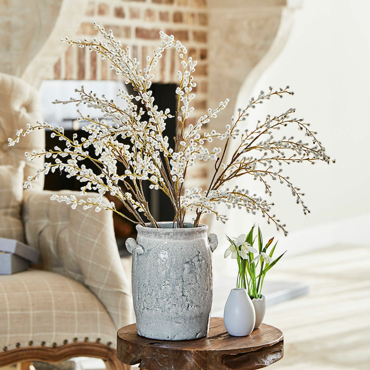 Set de 3 ramas decorativas Palmyra Jarrón de cerámica gris con ramas de amento sobre mesa de madera en sala luminosa