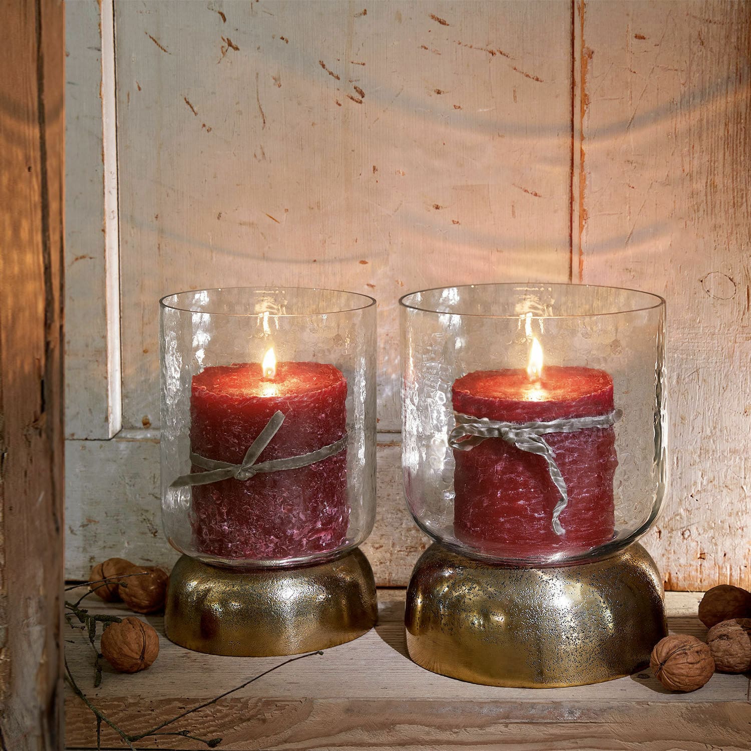 Set de 2 linternas Biserre Dos velas rojas en portavelas de vidrio con base dorada sobre fondo de madera rústica