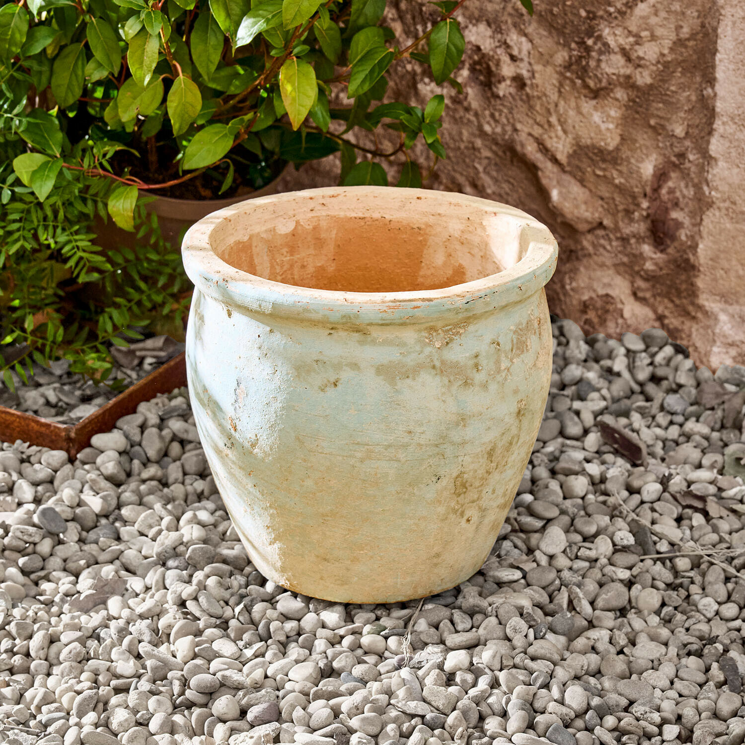 Macetero Naldorín Maceta grande de cerámica color beige claro sobre piedras en un jardín exterior