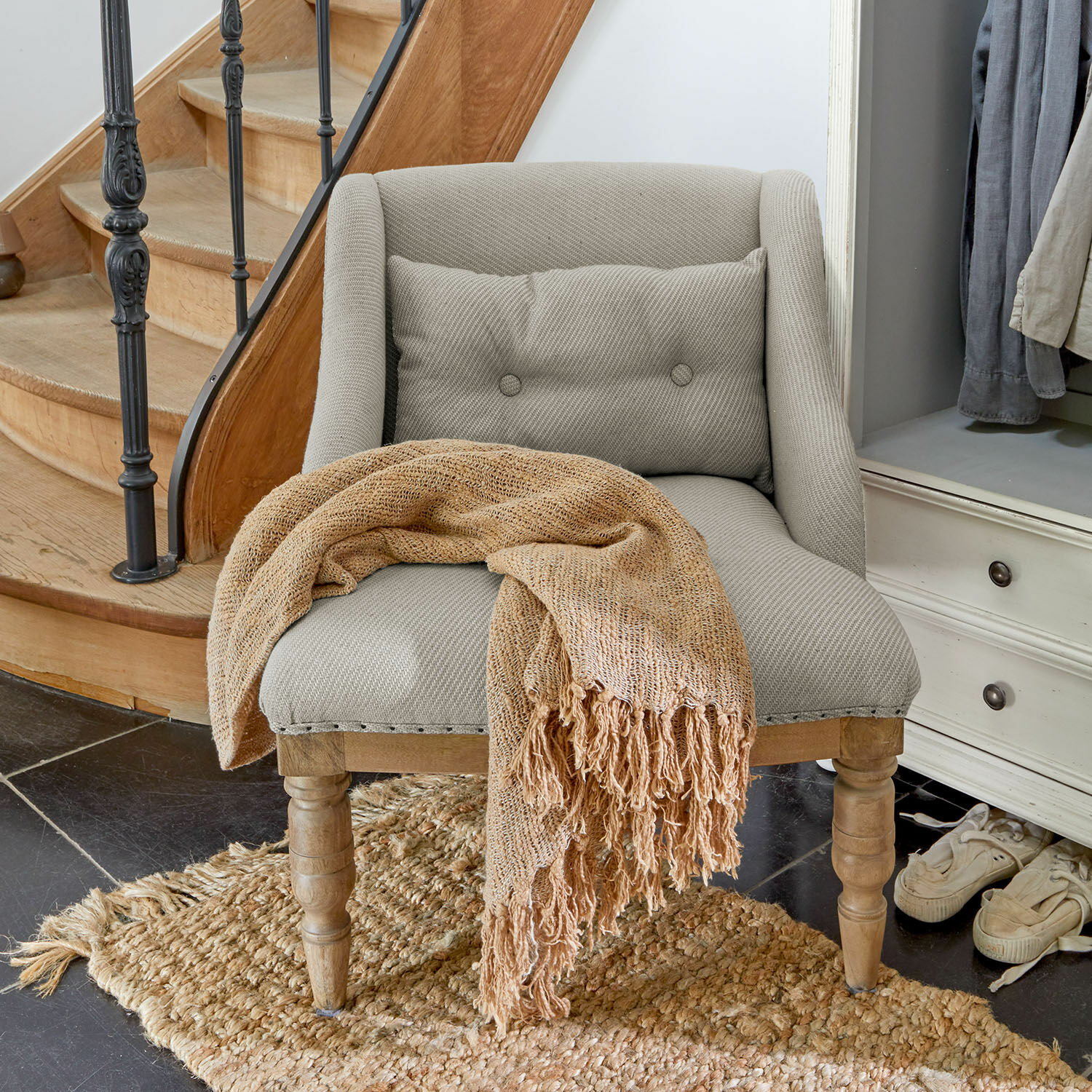 Sillón tapizado gris con patas de madera y manta beige tejida sobre alfombra de yute
