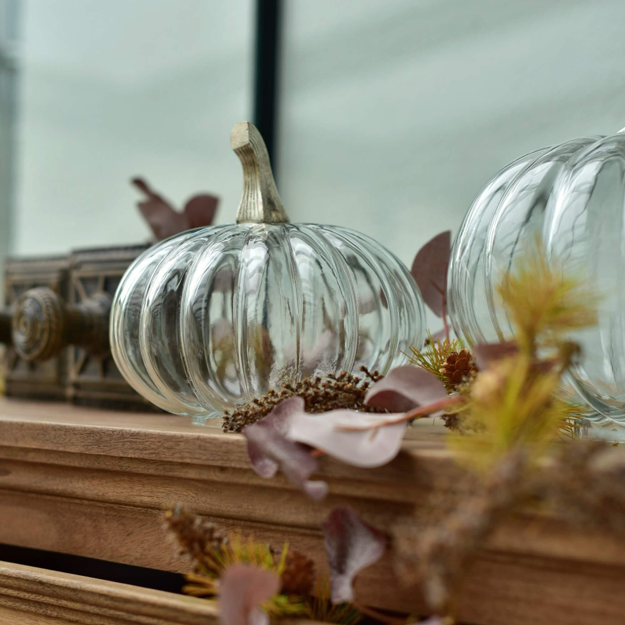 Calabaza de cristal transparente con tallo beige sobre superficie de madera con decoración otoñal