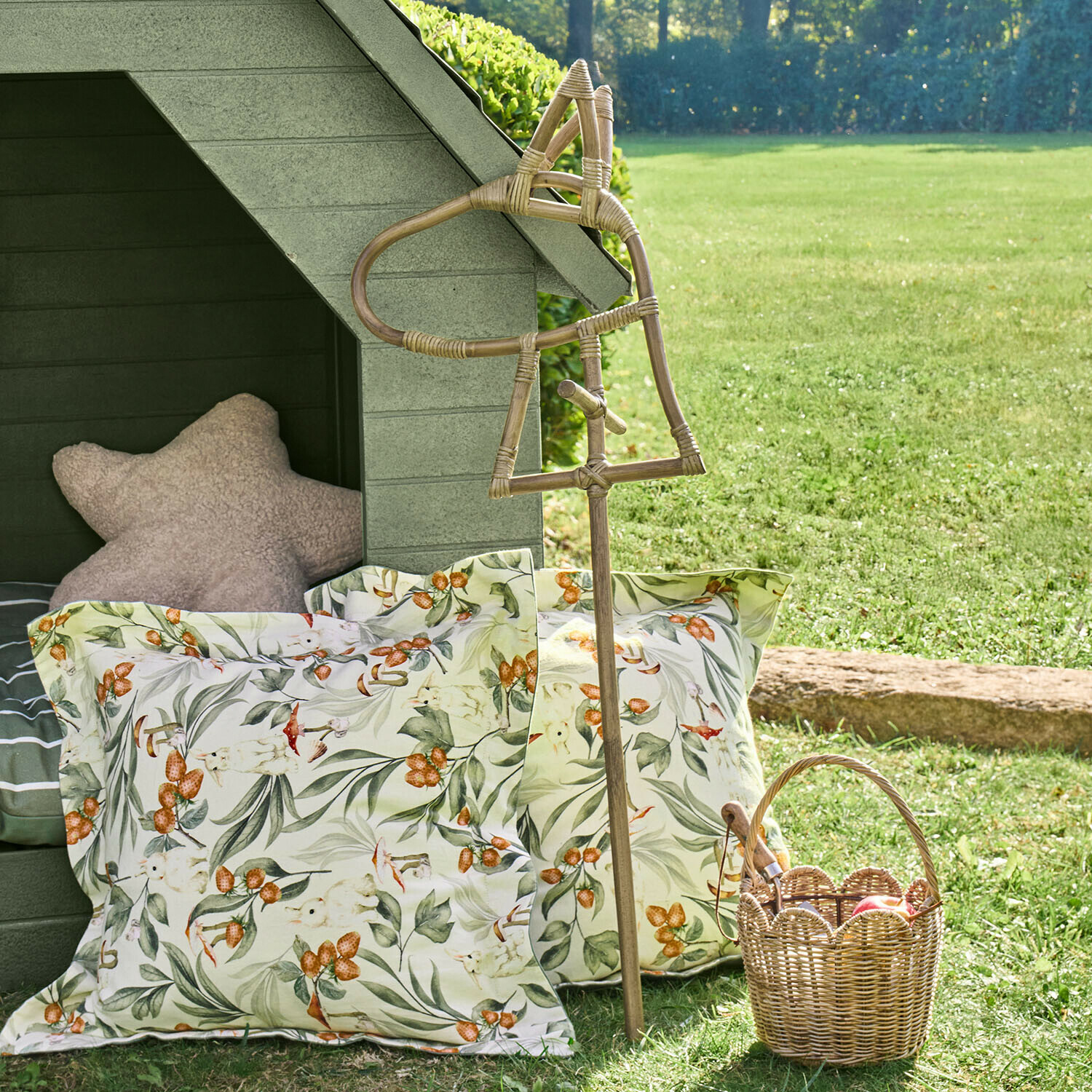 Caballo de palo Snokki Bastón decorativo de ratán con forma de caballo junto a cojines con estampado floral y cesta de mimbre