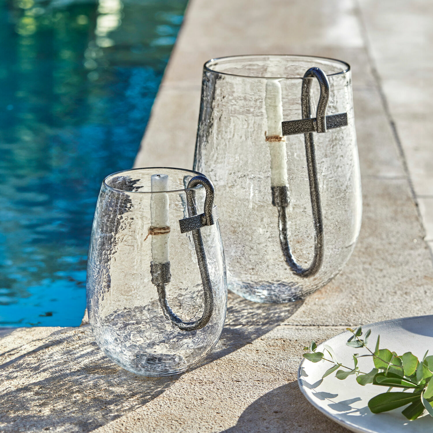 Set de 2 portavelas Lorcalla Faroles de vidrio con asa metálica y vela blanca junto a la piscina, decoración de jardín