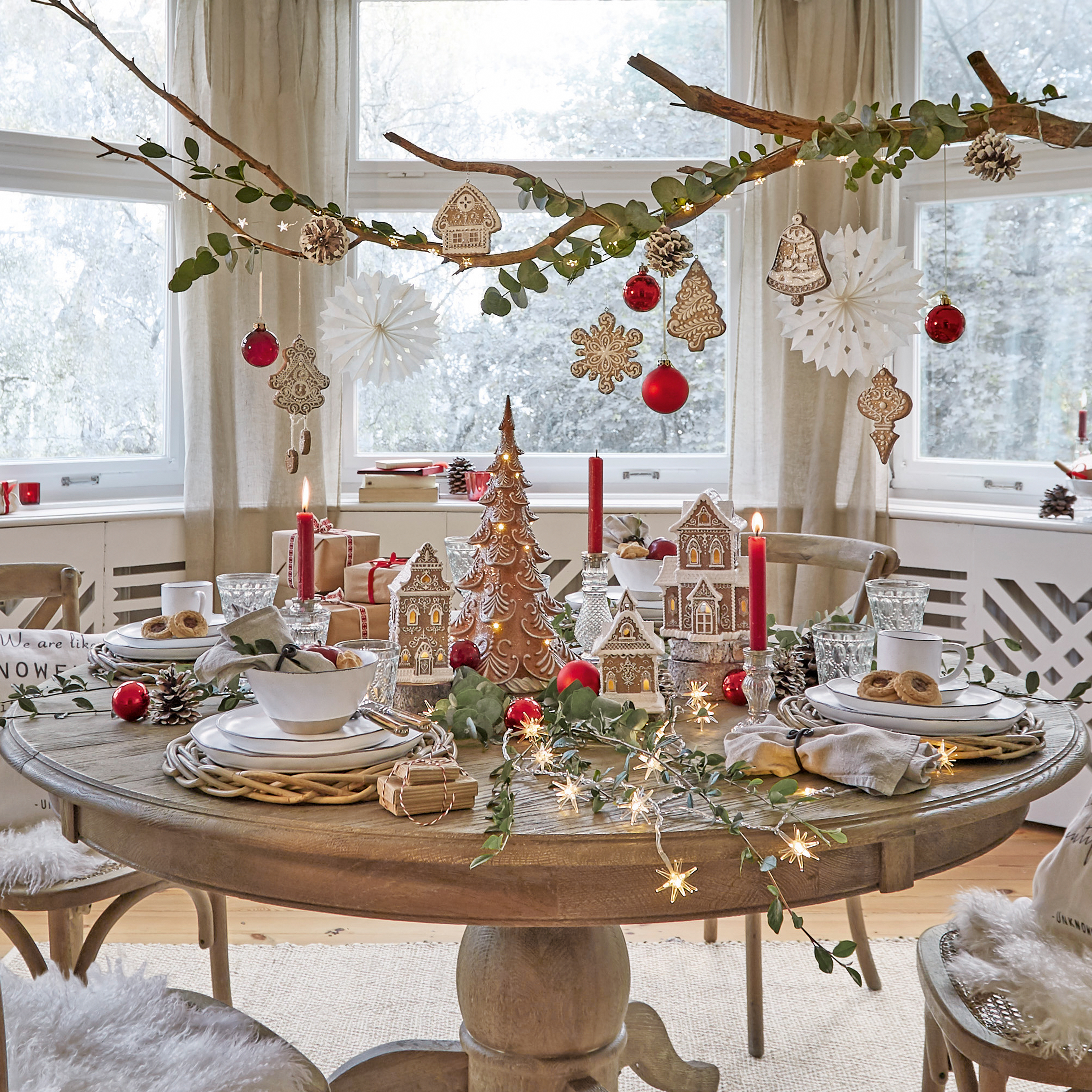 Mesa de madera redonda decorada con casas de jengibre, bolas rojas y velas encendidas para Navidad