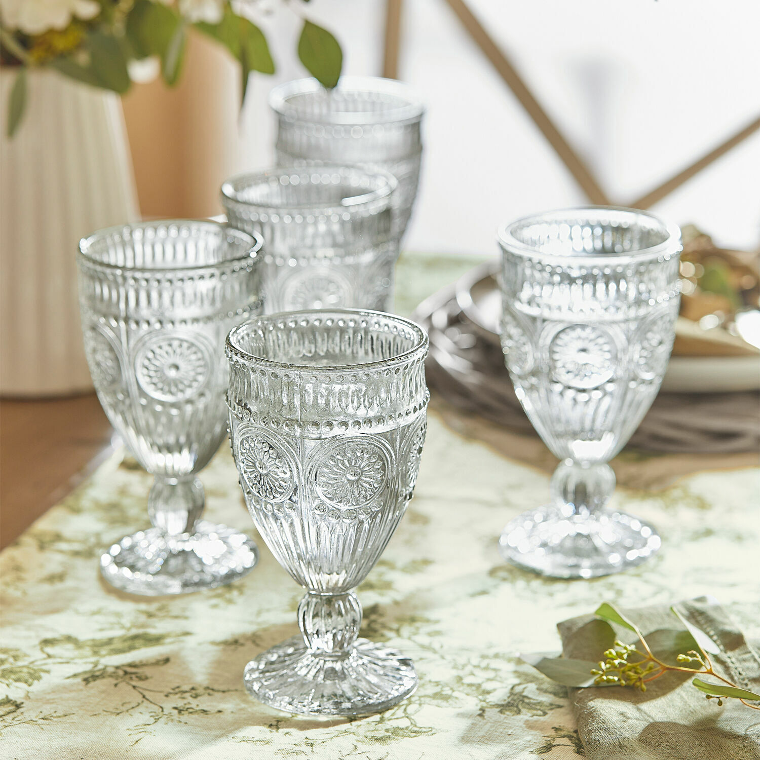 Set de 6 vasos Leatrice Conjunto de cinco vasos transparentes con diseño decorativo sobre mantel verde
