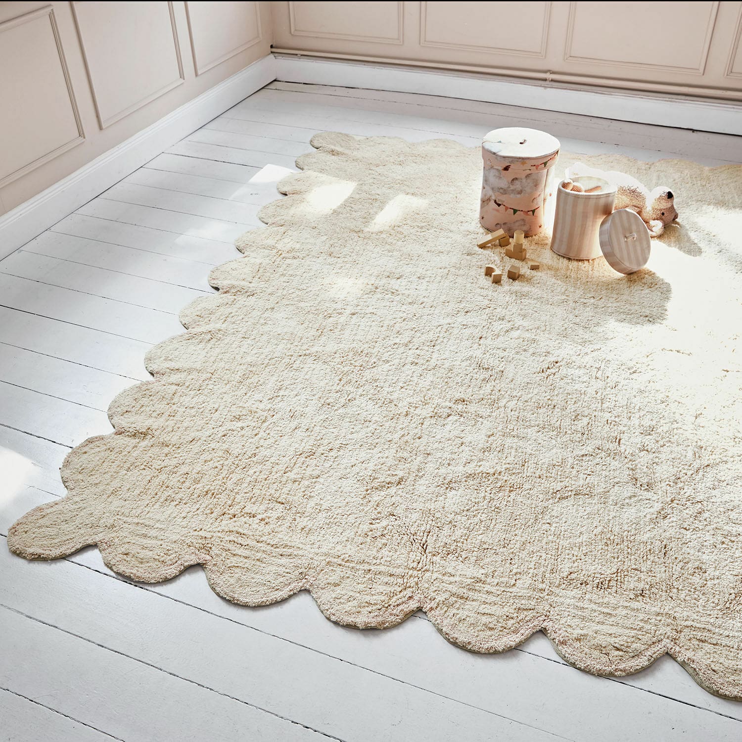 Alfombra Fenvara Alfombra beige de material suave con borde ondulado sobre suelo de madera clara en habitación infantil