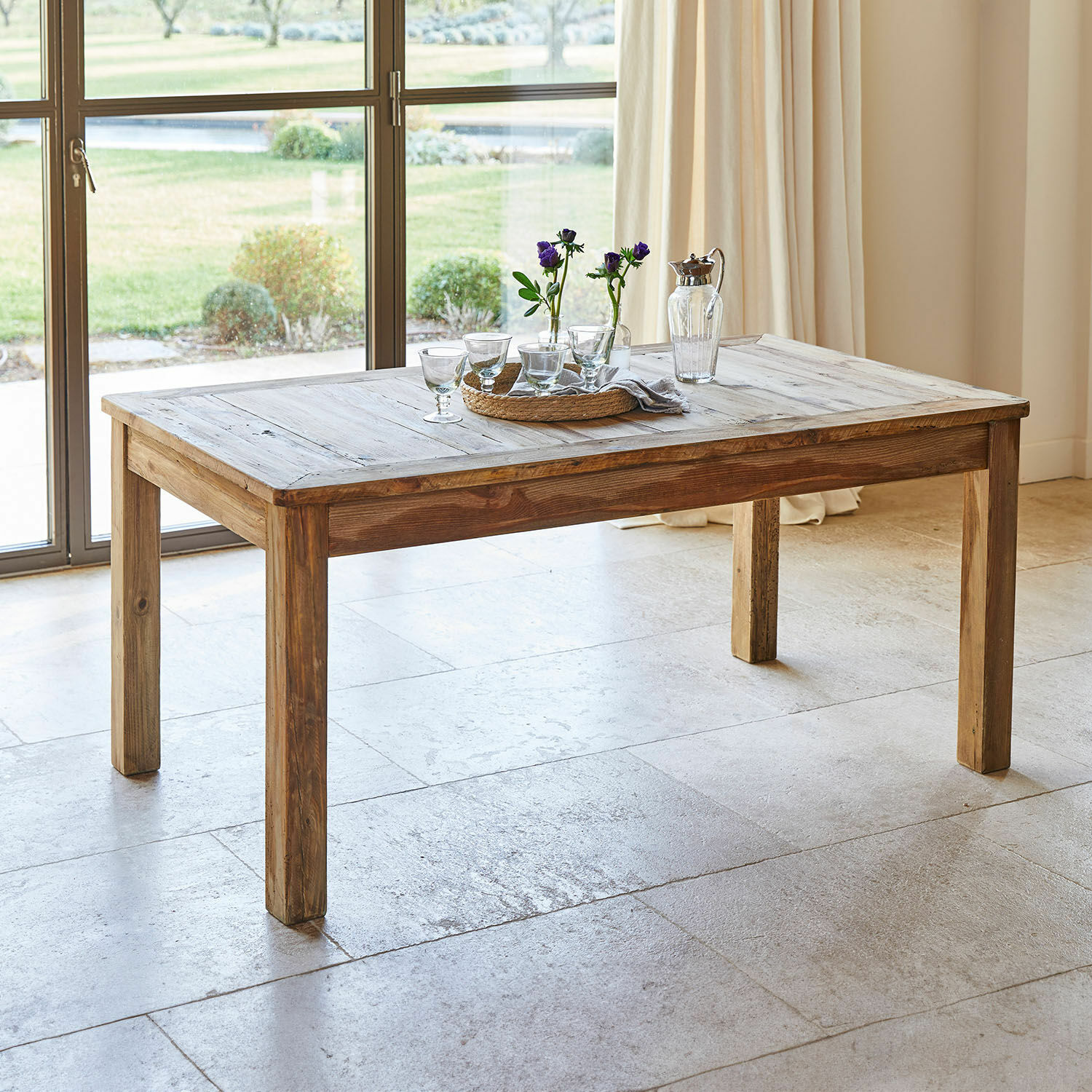 Mesa de comedor de madera natural con decoración de vasos y flores sobre la superficie en habitación luminosa