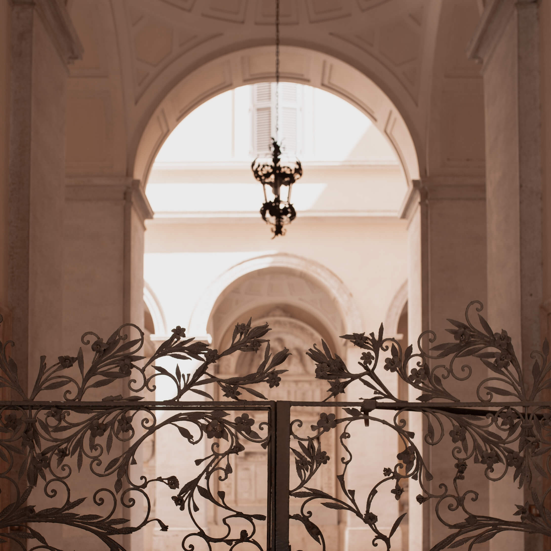 Puerta de hierro forjado decorada con motivos florales frente a un arco claro con lámpara colgante