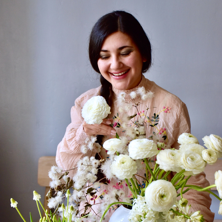 Mujer con blusa pastel arreglando flores blancas ranúnculo en jarrón, decoración primaveral