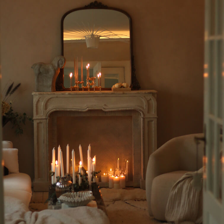 Sala acogedora con chimenea de piedra, espejo y varias velas encendidas que emiten luz cálida