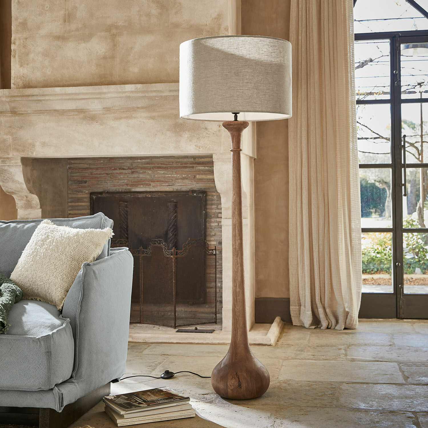 Lámpara de pie Andrées Lámpara de pie con base de madera y pantalla beige en sala acogedora con chimenea y sofá azul