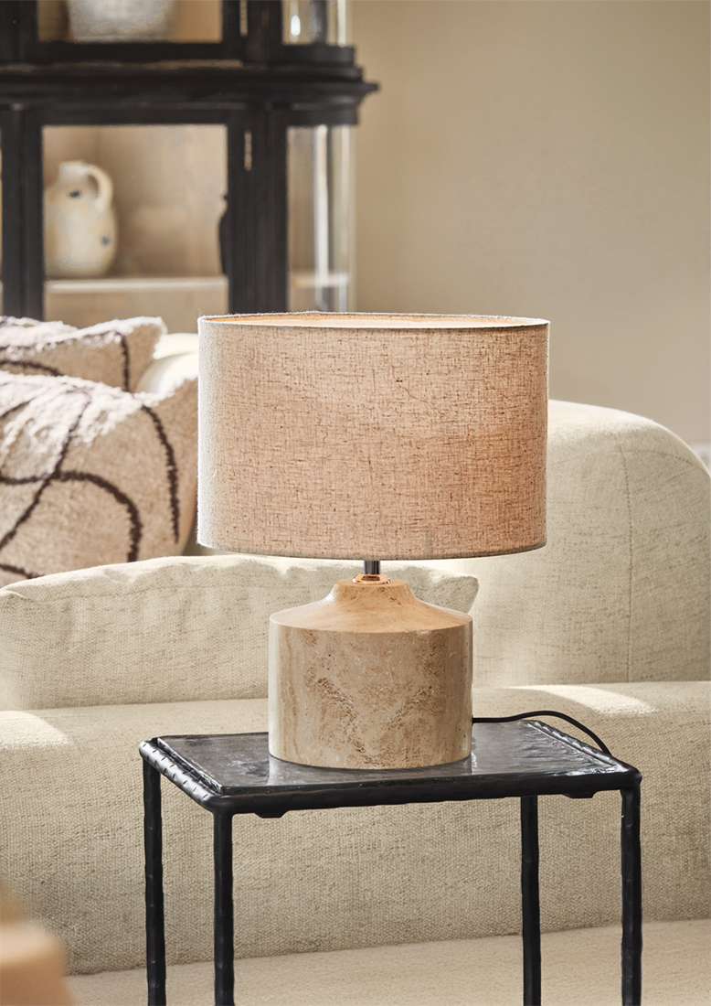 Lámpara de mesa con pantalla beige y base de cerámica color arena sobre mesa negra