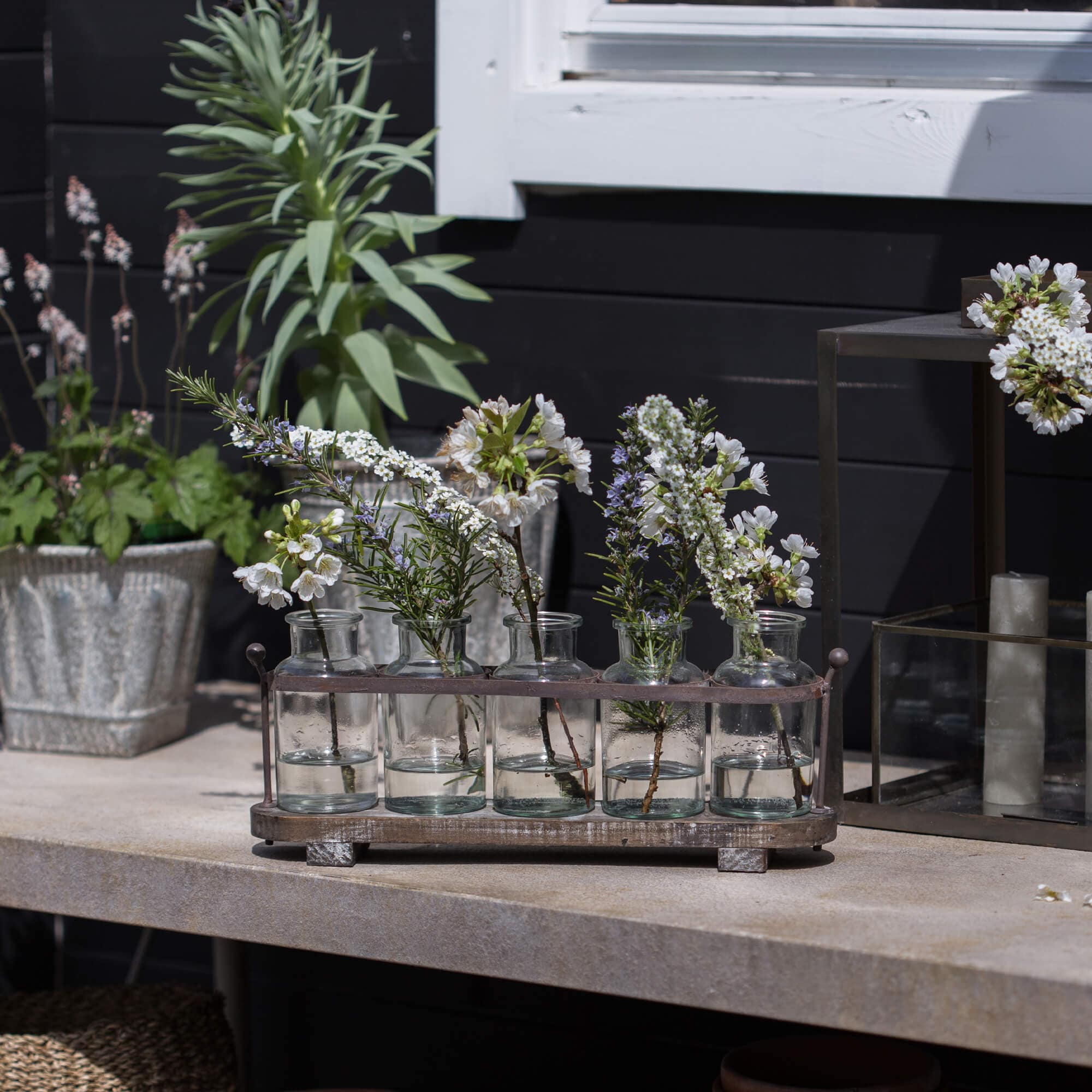 Botellas de vidrio con flores blancas en soporte metálico sobre mesa de piedra, decoración de jardín