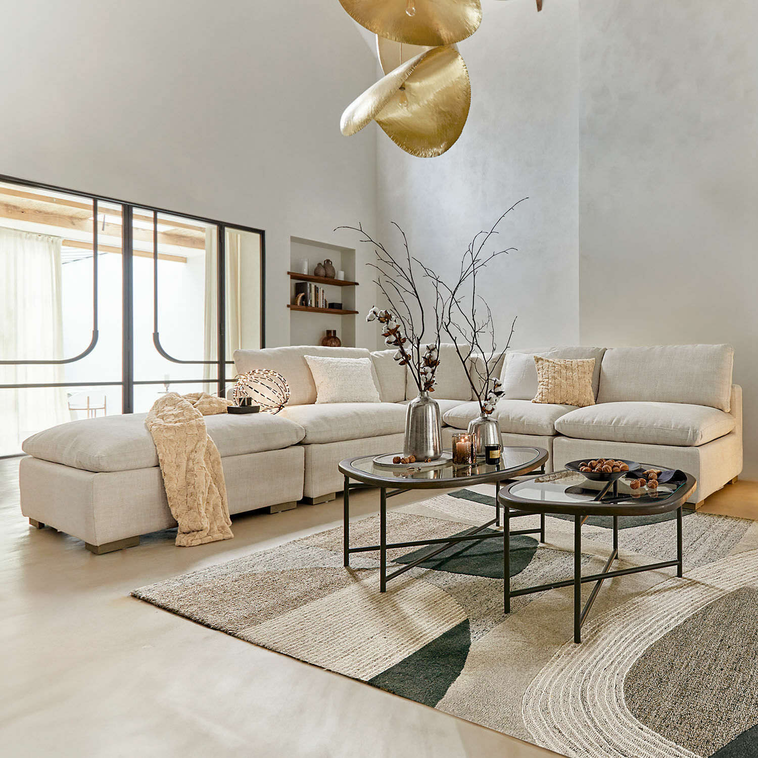 Sofá modular Baladou Sofá rinconero beige de tela en salón moderno con mesas de centro metálicas y decoración