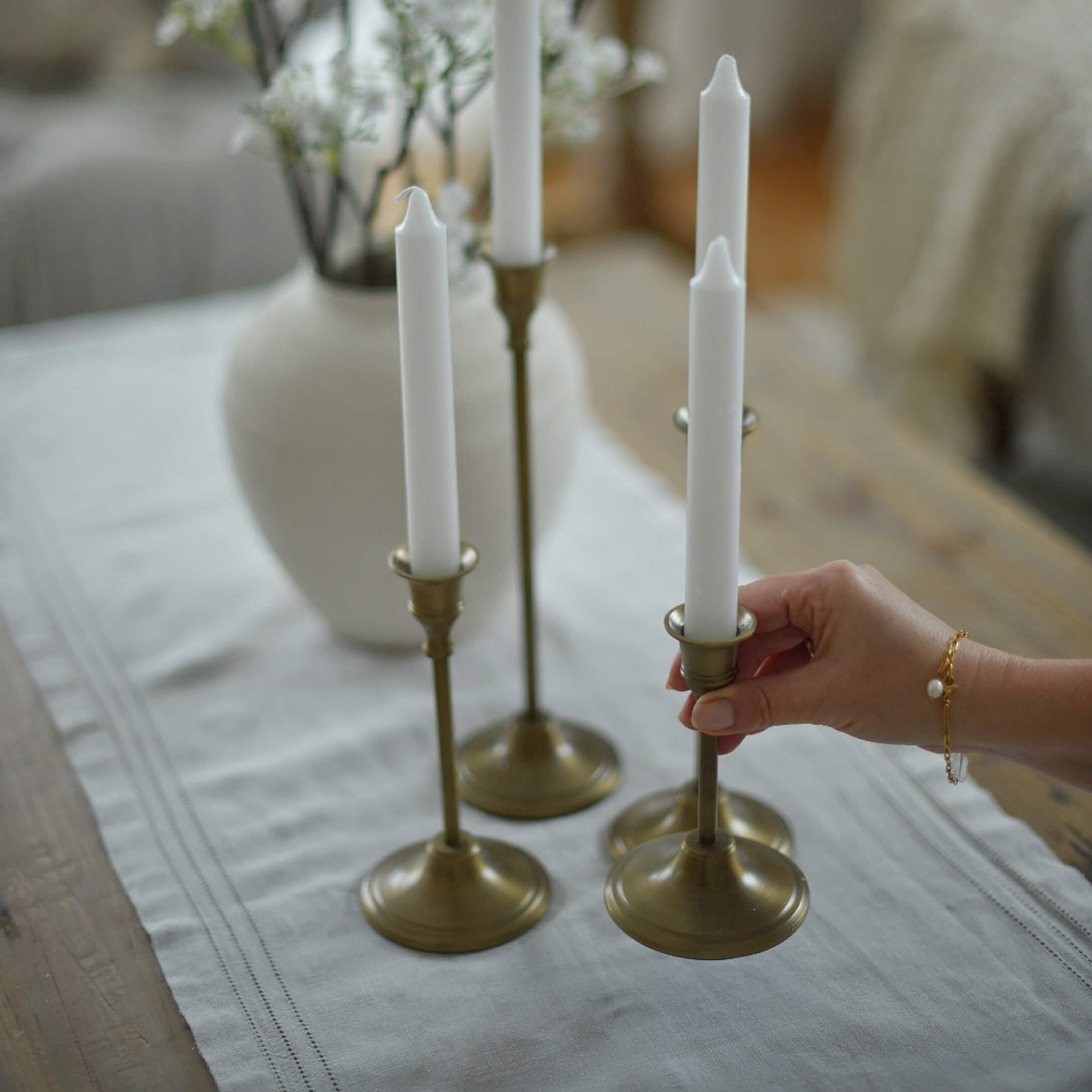 Conjunto de cuatro candelabros de latón con velas blancas sobre mantel de lino en ambiente acogedor