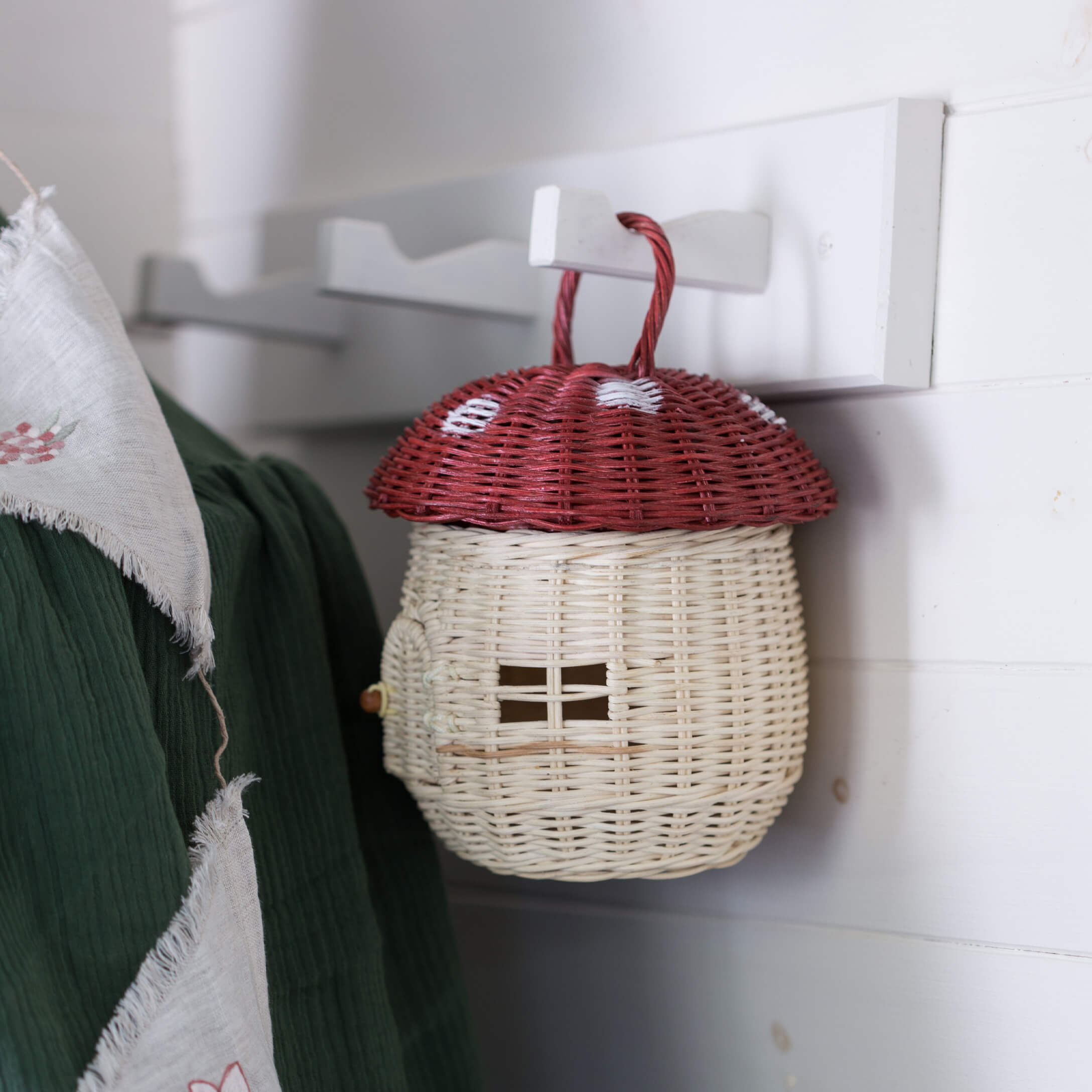 Cesta decorativa de mimbre con forma de hongo rojo con tapa roja y cuerpo blanco colgada de un gancho