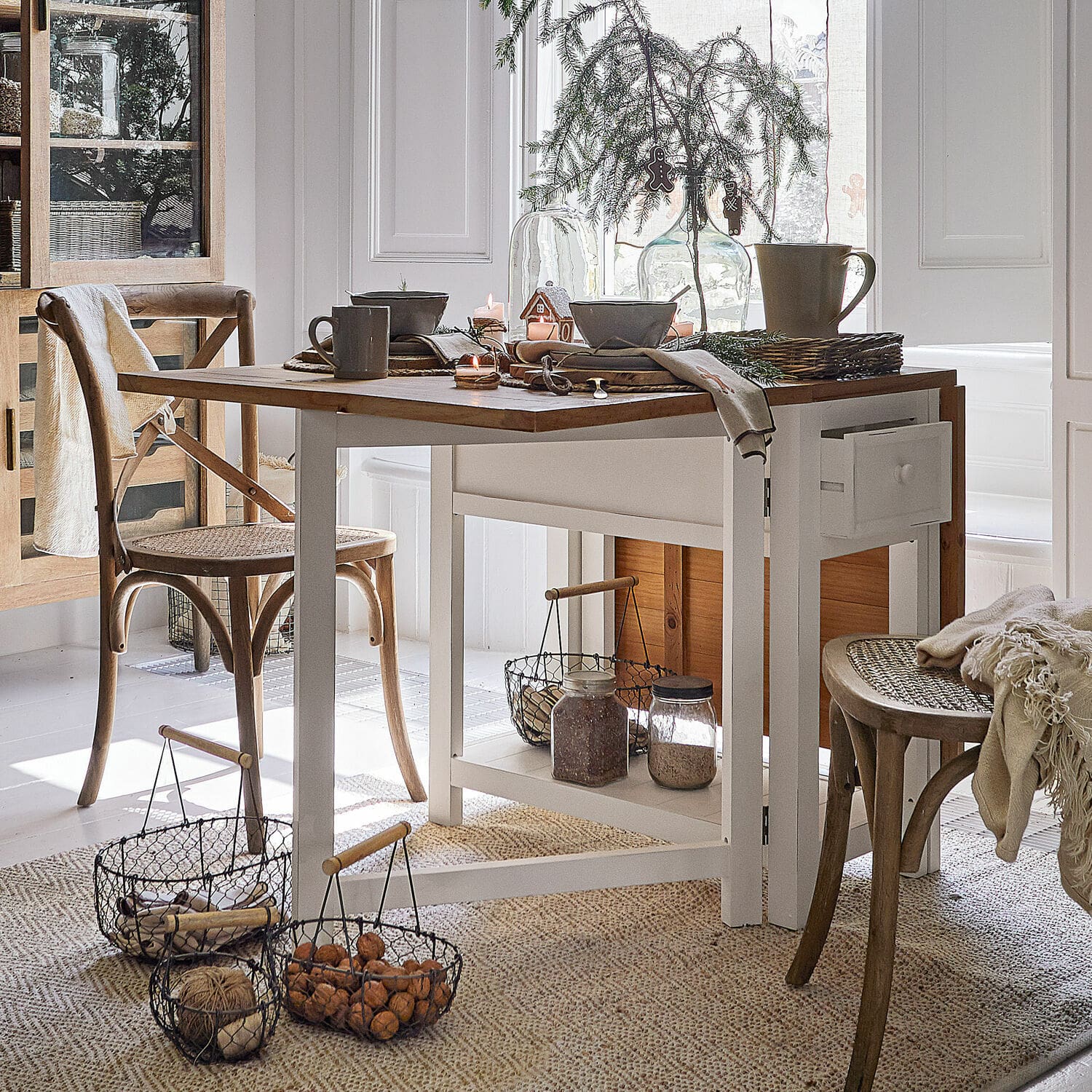 Mesa Dale Comedor con mesa de madera blanca y sillas de mimbre natural, decoración navideña y cestas con nueces