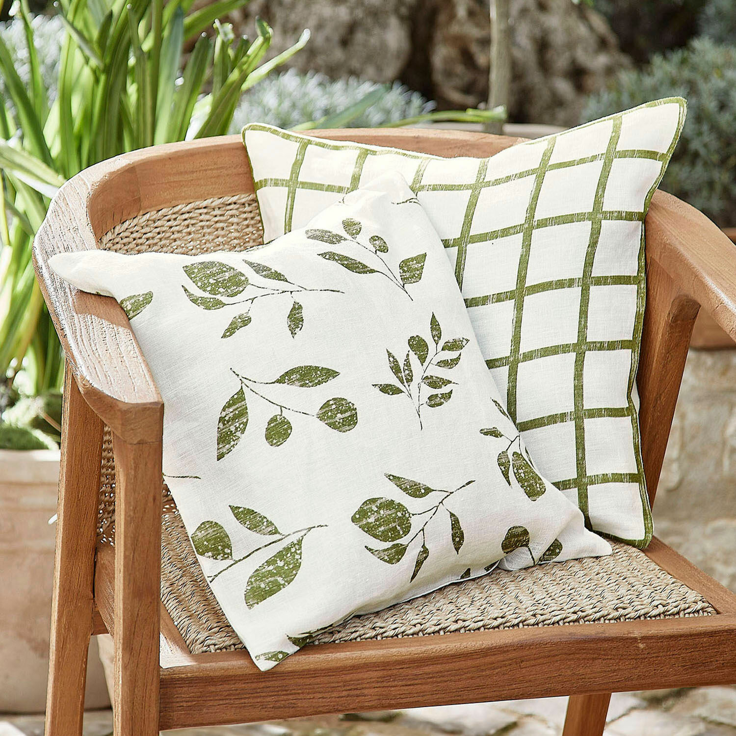 Set de 2 fundas de cojín Klivento Dos cojines de lino con hojas verdes y cuadros sobre una silla de madera en jardín