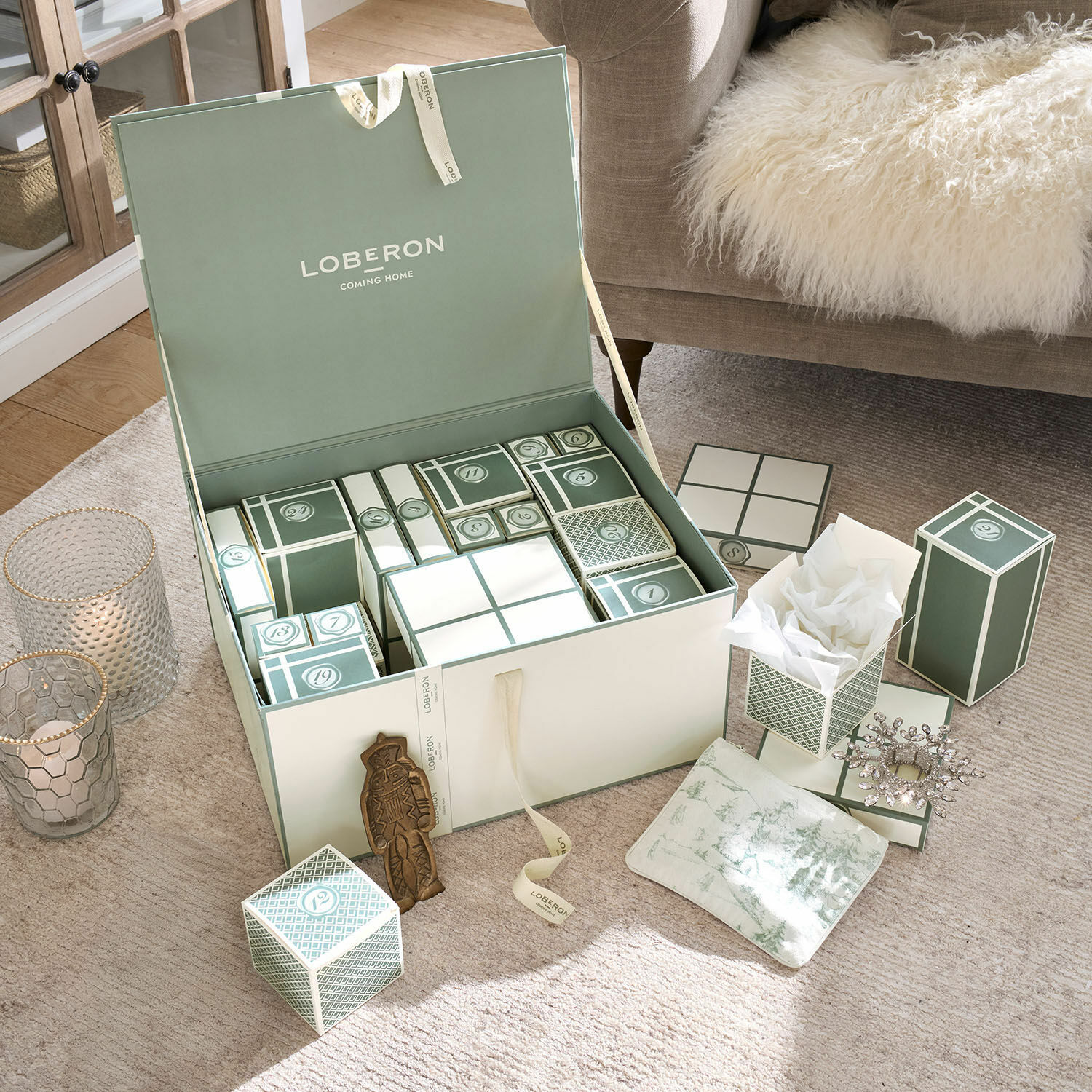 Calendario de Adviento Calavira Conjunto de cajas verdes y blancas de calendario de adviento sobre alfombra beige junto a sofá con manta de piel