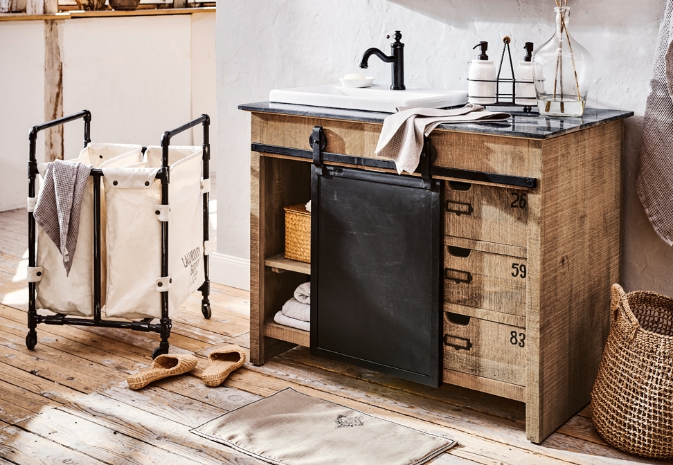 Baño industrial con mueble de madera, cajones metálicos negros y lavabo blanco sobre encimera de piedra