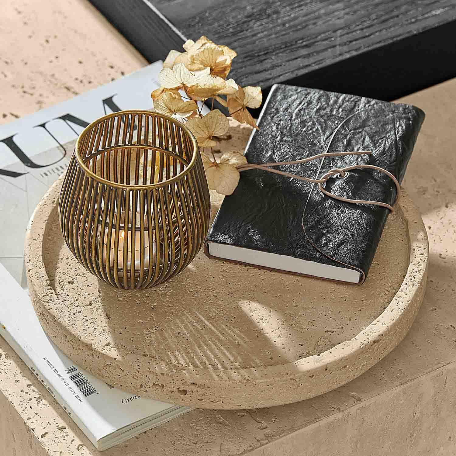 Bandeja redonda de piedra con cuaderno negro de cuero y farol dorado para vela sobre mesa