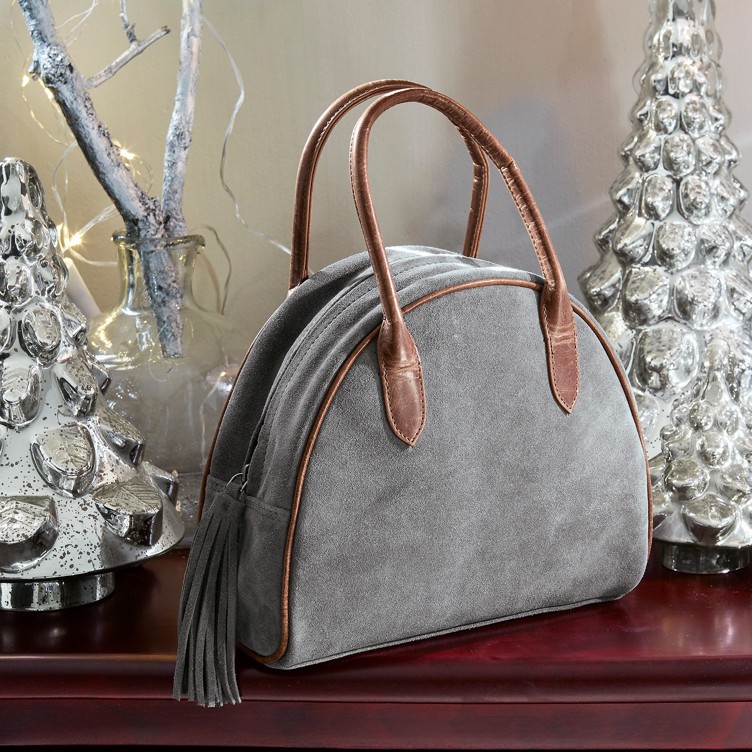 Bolso Elisabeta Bolso de ante gris con asas de cuero marrón y flecos sobre mesa con decoración navideña