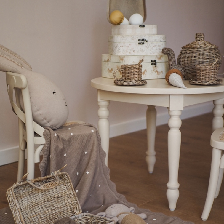 Mesa beige con juego de té de mimbre y cajas decorativas en habitación infantil acogedora