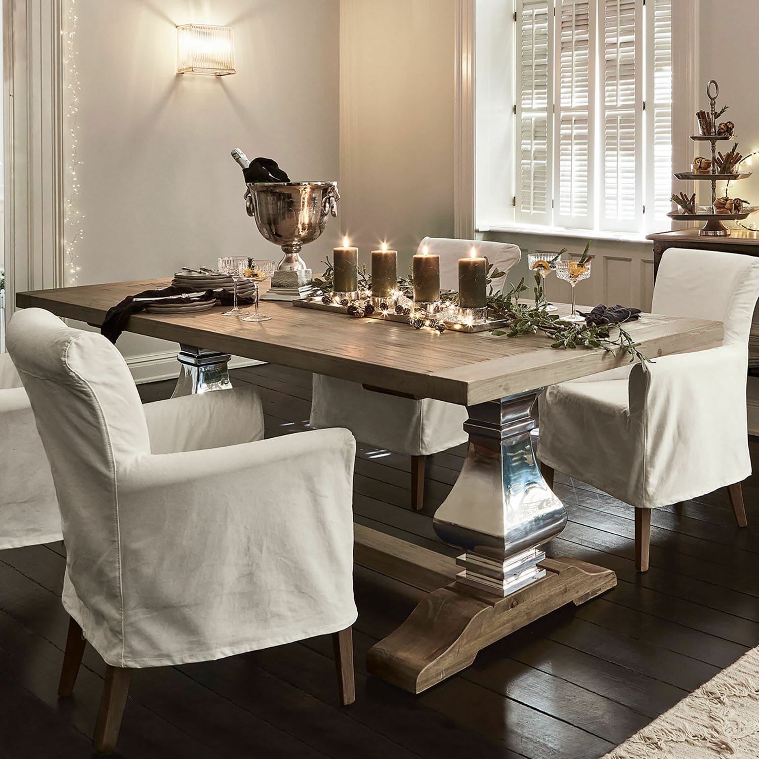 Mesa de comedor Filton Mesa de comedor de madera clara con patas metálicas y sillas con fundas blancas en interior elegante