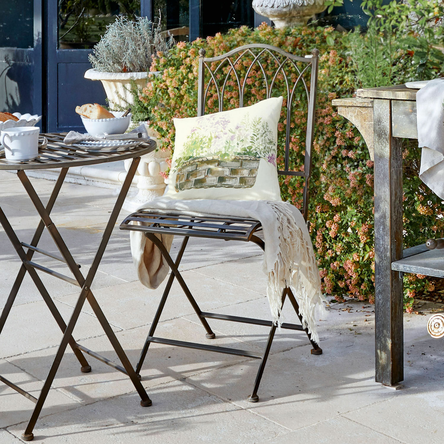 Mesa y silla plegables de metal marrón en terraza con cojín y manta decorativa