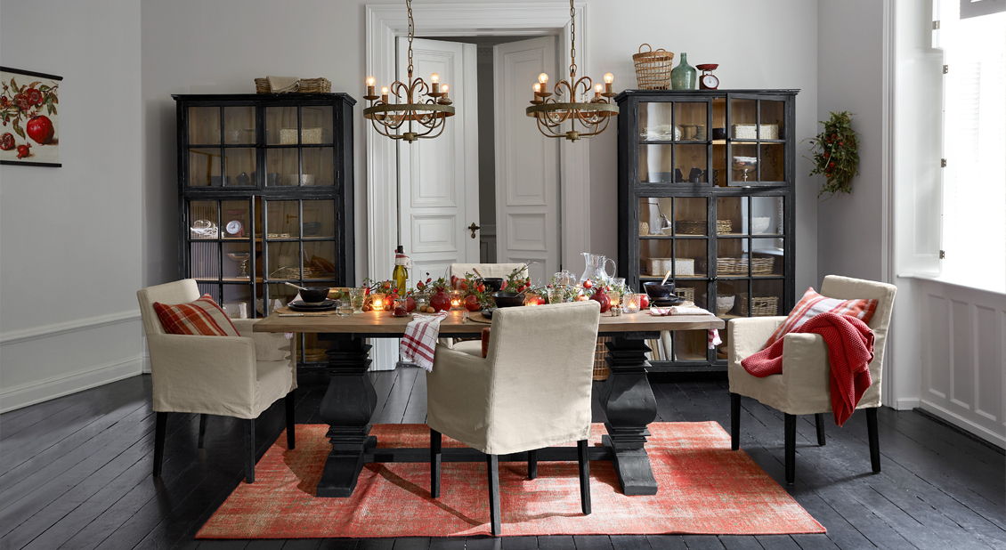 Comedor rústico con mesa de madera, sillas crema y vitrinas negras sobre paredes claras
