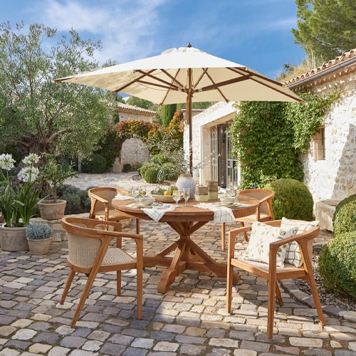 Mesa de jardín de madera con sombrilla y cuatro sillas sobre pavimento en patio soleado