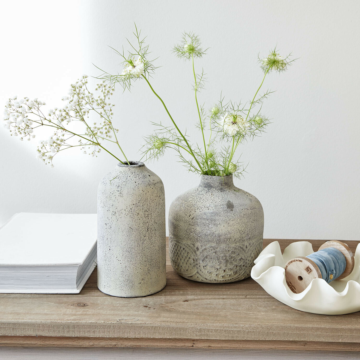 Set de 2 jarrones Vornelli Dos jarrones de cerámica gris con flores blancas delicadas sobre una mesa de madera clara