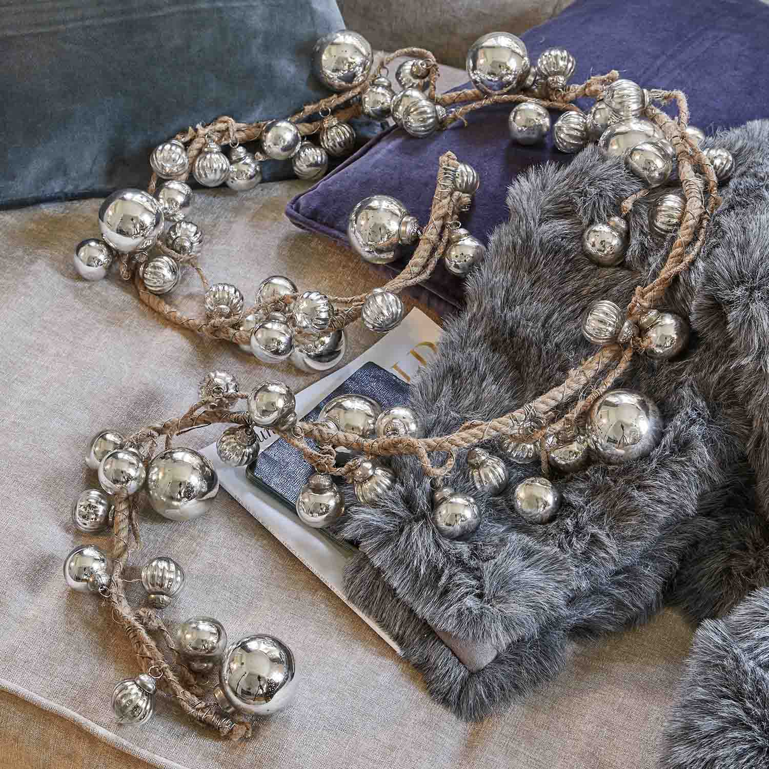 Guirnalda decorativa con bolas metálicas plateadas en cuerda de yute sobre cojines suaves y piel sintética