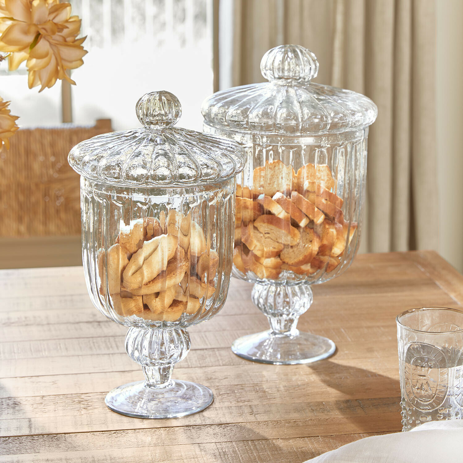 Set de 2 tarros de cristal Mélomiane Dos recipientes de vidrio transparente con tapas llenos de galletas sobre mesa de madera clara