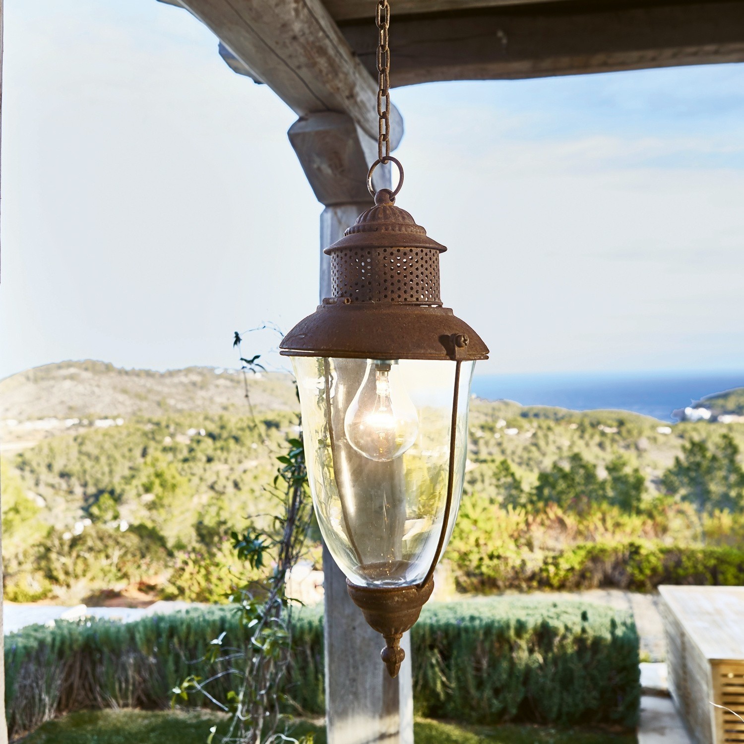 Farol colgante Floricia Lámpara colgante de metal oxidado y vidrio con vista a colinas verdes y mar en el fondo