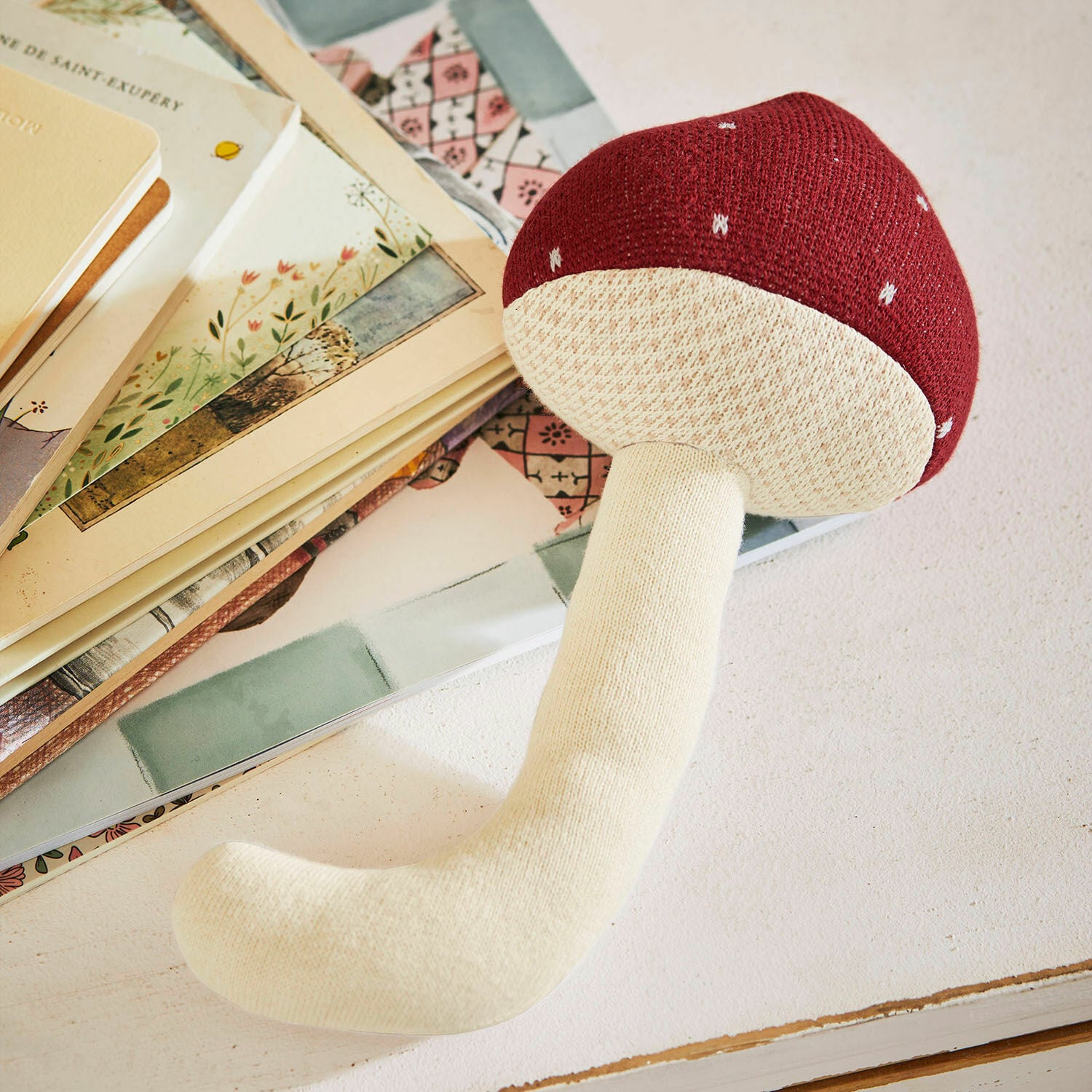 Seta textil Norilie Juguete de peluche en forma de hongo rojo y crema sobre mesa con libros