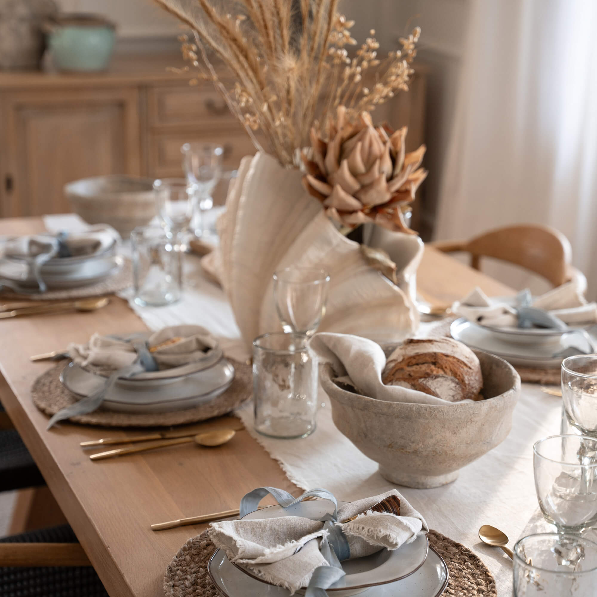 Mesa rústica de comedor con vajilla de cerámica y decoración natural de flores secas en camino de mesa