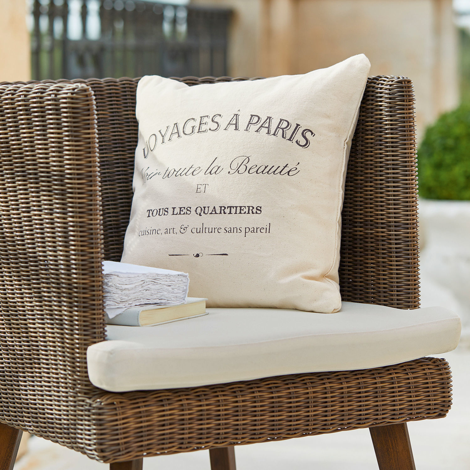 Cojín de algodón beige con estampado sobre sillón de mimbre marrón para jardín