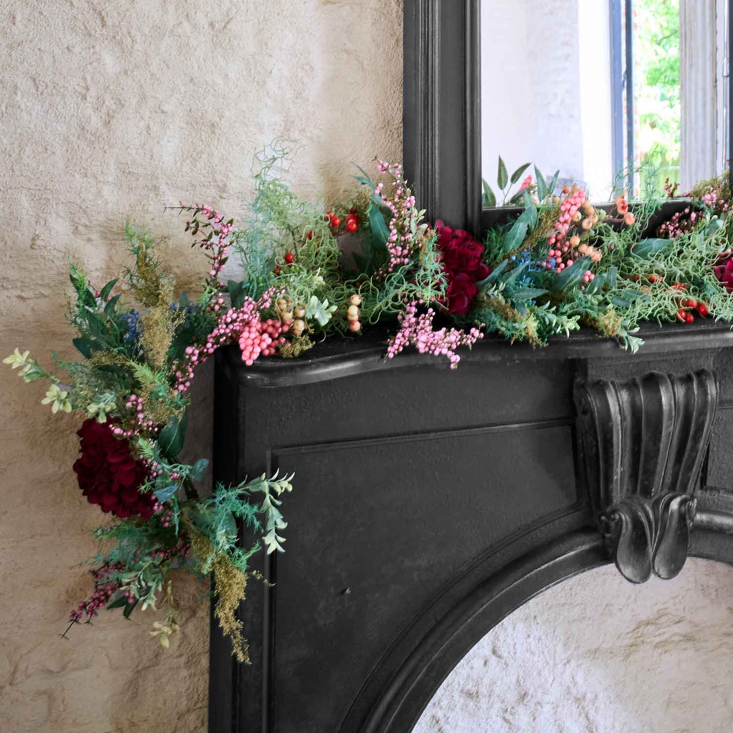 Guirnalda decorativa con bayas rojas y rosas y hojas verdes sobre chimenea negra